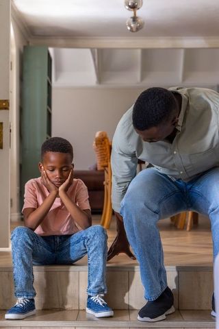 African american father helping son tie sneakers on home steps showing bond and care