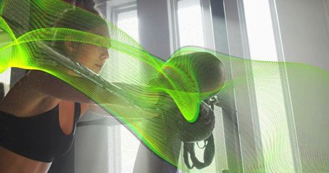 Female boxer striking heavy bag with neon green motion mesh overlay backlit gym workout