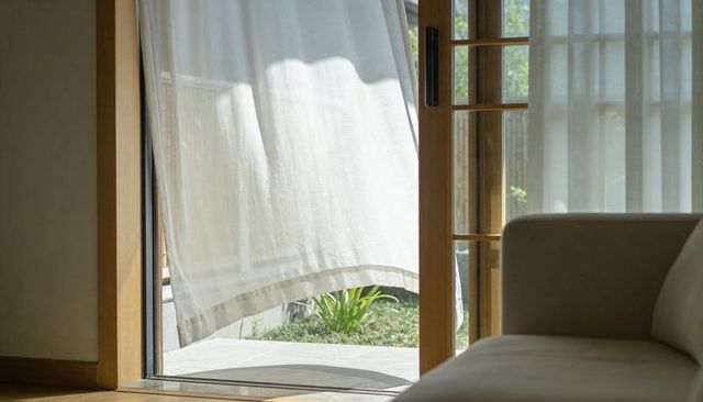 Billowing sheer curtain diffusing sunlight through wooden sliding door into calm living room