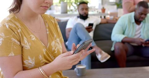 Woman texting on smartphone while relational moments occur in living room