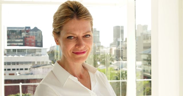 Professional businesswoman smiling confidently in a modern office environment with a city view, ideal for corporate, business, and professional themes. Useful for illustrating leadership, career success, and workplace settings.