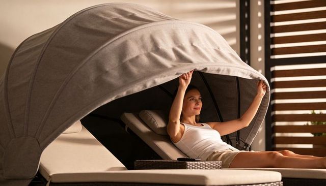 Woman lifting canopy over sun lounger while relaxing on modern outdoor patio daybed