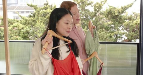Diverse women comparing summer dresses on balcony, choosing outfits for daytime event