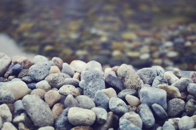 Vibrant pebbles on riverbank with blurred water in background. Great for nature scenes, relaxation themes, backgrounds, and textures.
