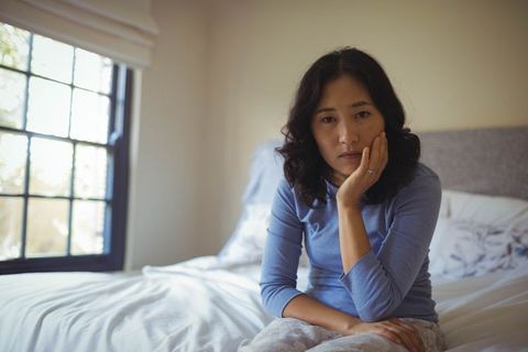 Thoughtful woman sitting on bed in cozy bedroom interiors