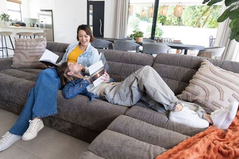 Two women lounging and reading on grey sectional sofa in bright modern living room