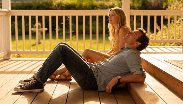 Couple relaxing on sunlit porch at golden hour, woman in yellow sundress, man in denim