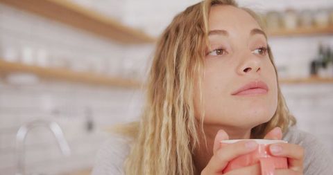 Woman contemplating while drinking tea in modern kitchen