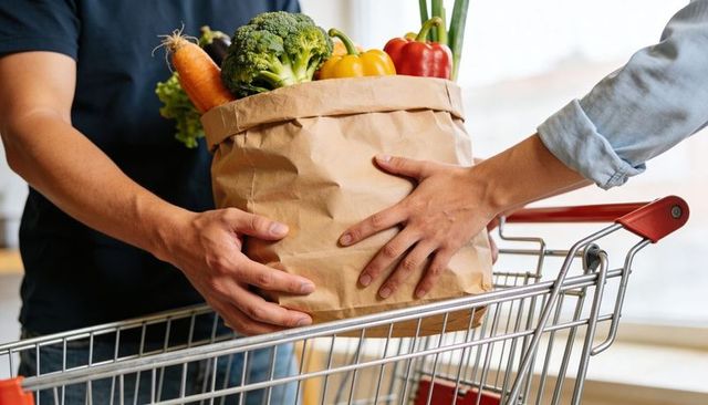 Couple transferring fresh groceries into shopping cart with colorful vegetables