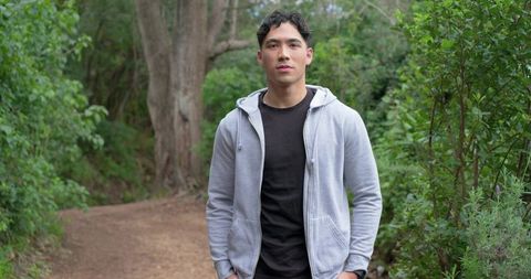 Young man standing on forest trail wearing gray hoodie wristwatch casual outdoor portrait