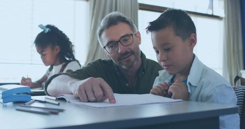 Male Tutor Guiding Young Boy With Homework