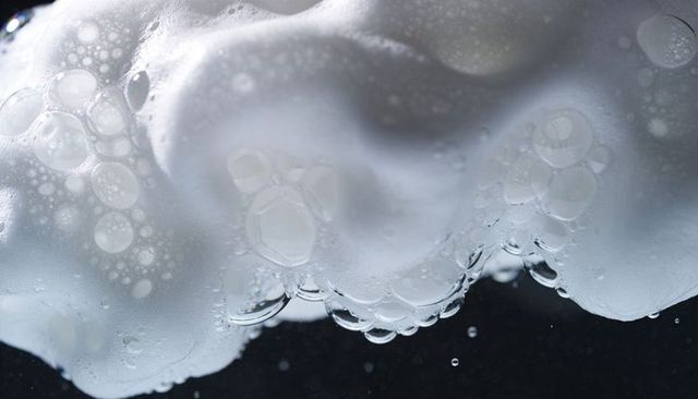 Bubbling white foam forming glossy soap bubbles and iridescent droplets macro texture