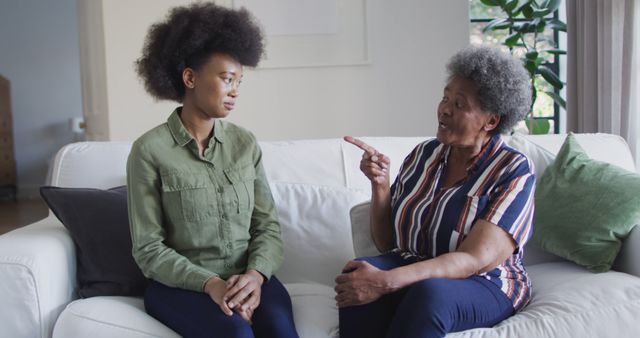 Elderly woman giving advice to young woman while sitting on sofa in living room. Ideal for content about family relationships, intergenerational communication, advice and support, emotional well-being, and home settings.