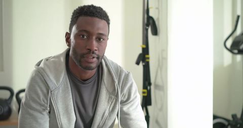 Mid adult african american man sitting in gym wearing gray hoodie with kettlebells, trx