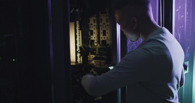 IT technician working on server equipment in dimly lit data center, highlighting technical support and maintenance in the technology industry. Perfect for illustrating concepts related to IT services, data management, network security, or computer hardware maintenance.