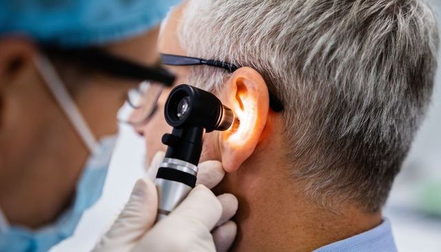Clinician examining elderly patient ear with otoscope light for hearing check and diagnosis