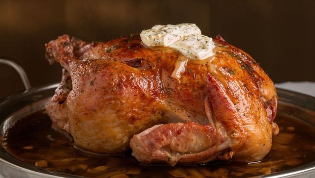 Golden roasted whole chicken topping melting herb butter and glossy pan juices