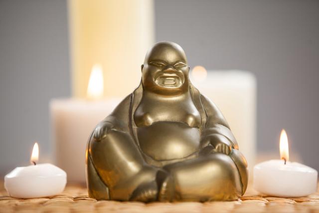 Gold painted laughing buddha figurine and lit candles on mat