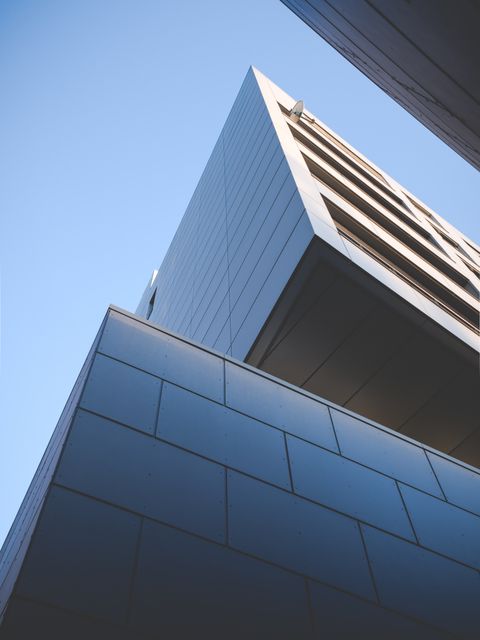 Depicts a modern urban building featuring clean lines and geometric shapes, set against a clear blue sky. Ideal for use in commercial real estate, architectural design projects, urban development presentations, or modern lifestyle magazines.