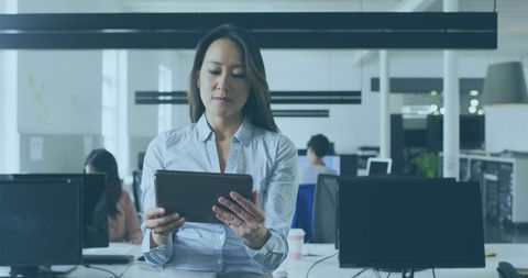 Professional Woman Reviewing Tablet While Standing in Modern Open-Plan Office Workspace