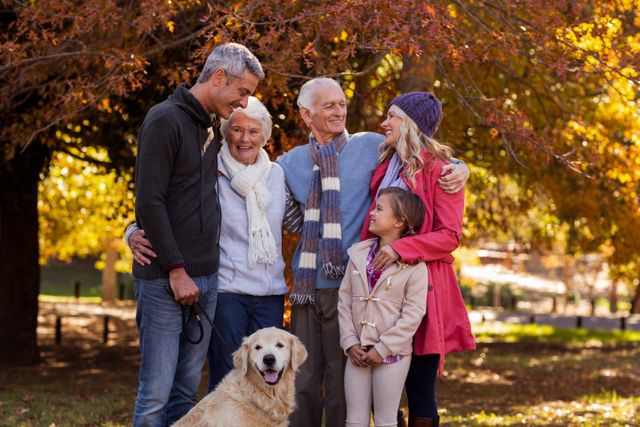 This image shows a multi-generation family enjoying a day at the park during autumn. The family includes grandparents, parents, and a child, all smiling and bonding together. The golden retriever adds a touch of warmth and companionship. The fall foliage in the background creates a beautiful seasonal atmosphere. This image is perfect for use in advertisements, family-oriented content, seasonal promotions, and articles about family bonding and outdoor activities.