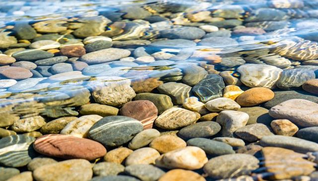 Shimmering river pebbles under clear water with sunlit caustic ripples