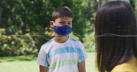Young boy wearing blue face mask standing and talking with friend outdoors in garden