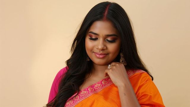 Smiling indian woman wearing orange saree with pink border and jhumka showing sindoor