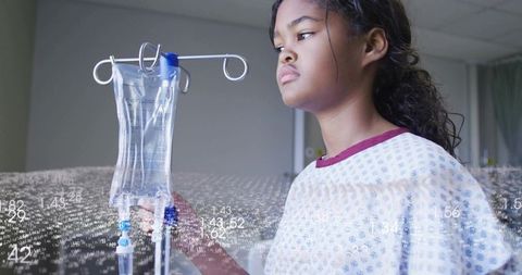Young patient touching IV drip in pediatric ward in gown with digital medical data overlay