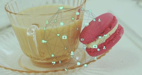 Glass teacup with creamy latte and pink macaron with teal digital network overlay