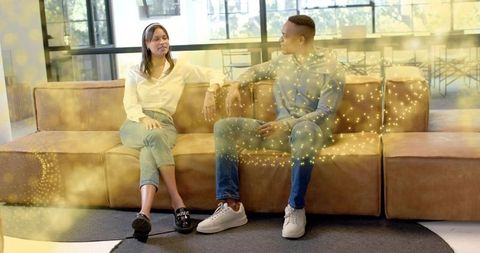 Colleagues chatting on brown leather sofa in bright coworking lounge, casual collaboration