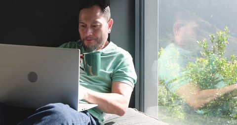 Asian Man Working with Laptop and Coffee in Sunlit Home Office