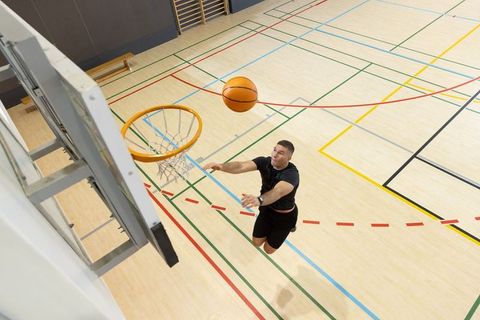Explosive basketball layup athlete jumping toward hoop on indoor hardwood court