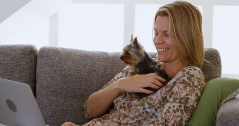 Caucasian Woman Relaxing on Couch with Laptop and Pet Dog