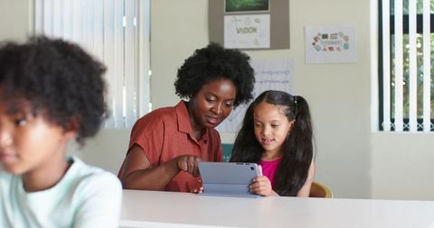 African American Tutor Teaching Elementary Girl Using Tablet in Bright Classroom
