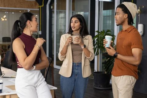 Diverse team chatting and collaborating over coffee during break in modern open-plan office