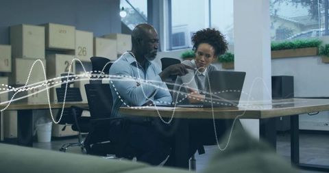 Collaborating professionals pointing at laptop analyzing data in modern open office