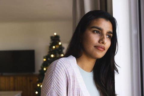 Woman by window in cozy living room with christmas tree