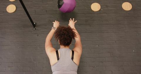 African american woman throwing purple medicine ball against brick wall for workout