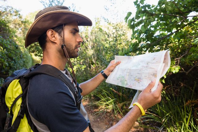 Man exploring forest trail, using map for navigation. Ideal for themes of adventure, outdoor activities, travel, and nature exploration.