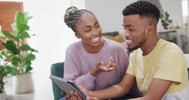 Young African American couple enjoying time together while using a digital tablet in a cozy living room. Ideal for content related to modern relationships, technology at home, leisure activities, and family bonding.
