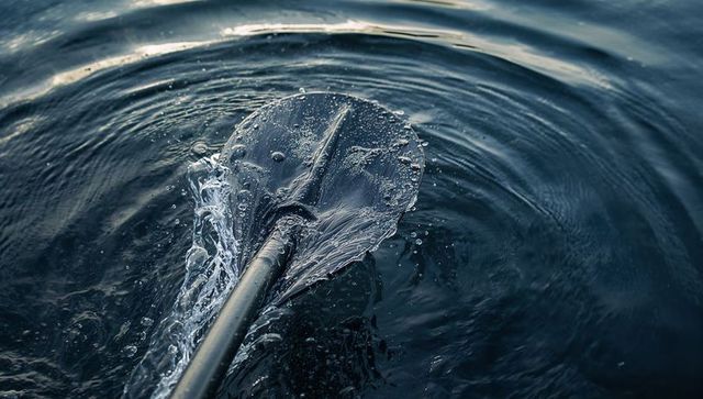 Paddle blade slicing dark blue water with splashing droplets and ringing ripples