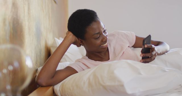 African american woman smiling and using smartphone alone in her bedroom - Download Free Stock Photos Pikwizard.com