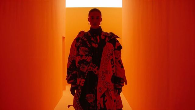 Backlit Fashion Model Posing in Minimalist Orange Corridor Wearing Oversized Graphic Coat