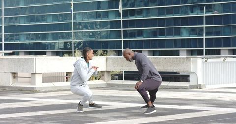 Urban rooftop fitness session with diverse men squatting and coaching in athletic wear