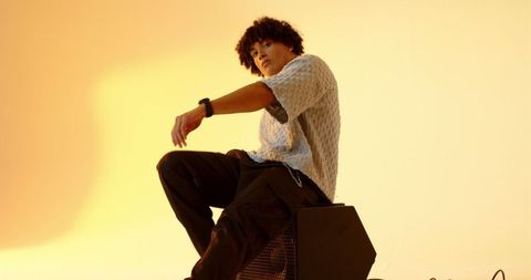 Stylish man in minimalist fashion sitting on cube with yellow background