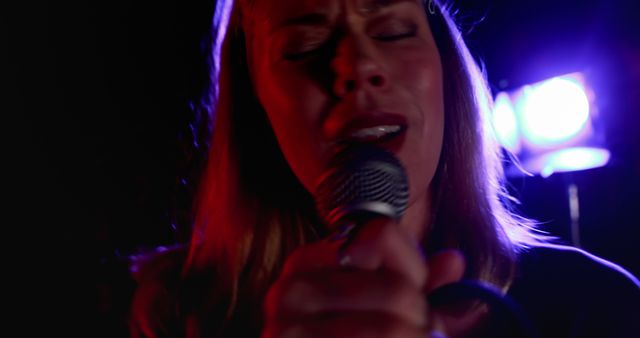 Young Caucasian woman sings passionately on stage, with copy space. Her intense performance highlights the vibrant atmosphere of live music events.