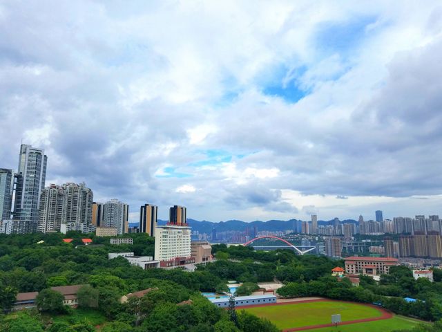 Includes an urban cityscape blending modern high-rise buildings and lush green areas under a cloudy sky. Visible athletic stadium suggests recreational activities, highlighting harmony between urban living and nature. Useful for concepts like urban planning, real estate, environmental balance, and leisure activities.