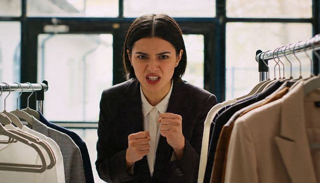 Angry asian businesswoman clenching fists in boutique showroom between clothing racks