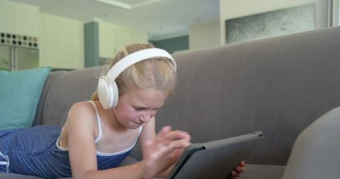 Girl lying on sofa learning with tablet and headphones at home
